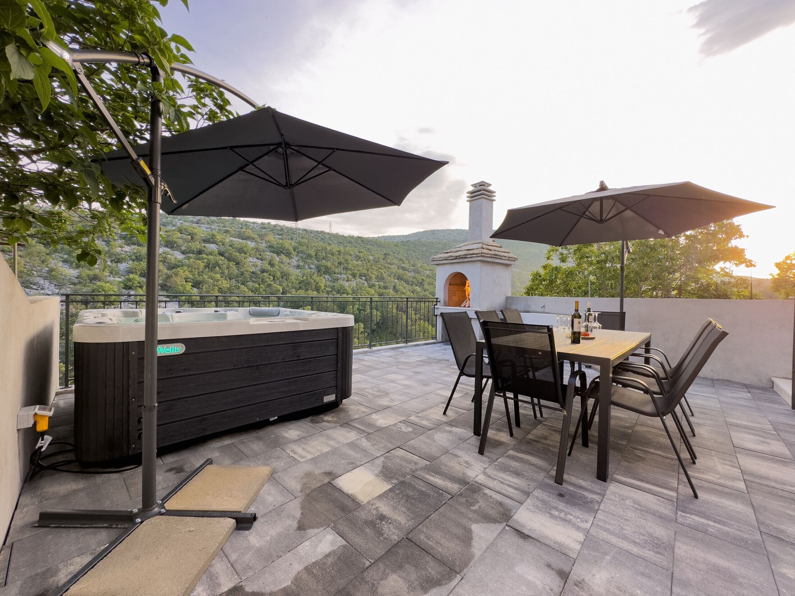 Un patio exterior con un jacuzzi, una mesa con sillas y sombrillas.
