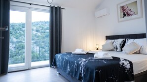 Ein Schlafzimmer mit einem Bett, einem Nachttisch, einem Fenster mit Vorhängen, einer Wand-Klimaanlage und einem Bilderrahmen.