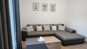 Ein modernes Wohnzimmer mit einem grauen Ecksofa, einem Holztisch und drei gerahmten Pflanzenbildern an der Wand.