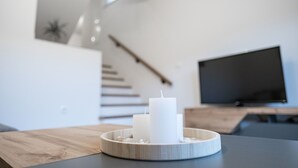 Ein modernes Wohnzimmer mit einem Holztisch, der zwei weiße Kerzen, einen Flachbildfernseher und eine Treppe im Hintergrund beherbergt.
