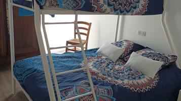 A bunk bed with a patterned bedspread and pillows, a wooden chair, and a window with curtains.