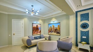 A living room with a beige sofa, two armchairs, a round rug, and two paintings on the wall. - Samaria Hotel and Spa (Samarkand)