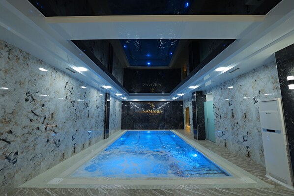 Une piscine intérieure aux murs et au plafond en marbre, entourée d’un couloir au design moderne.