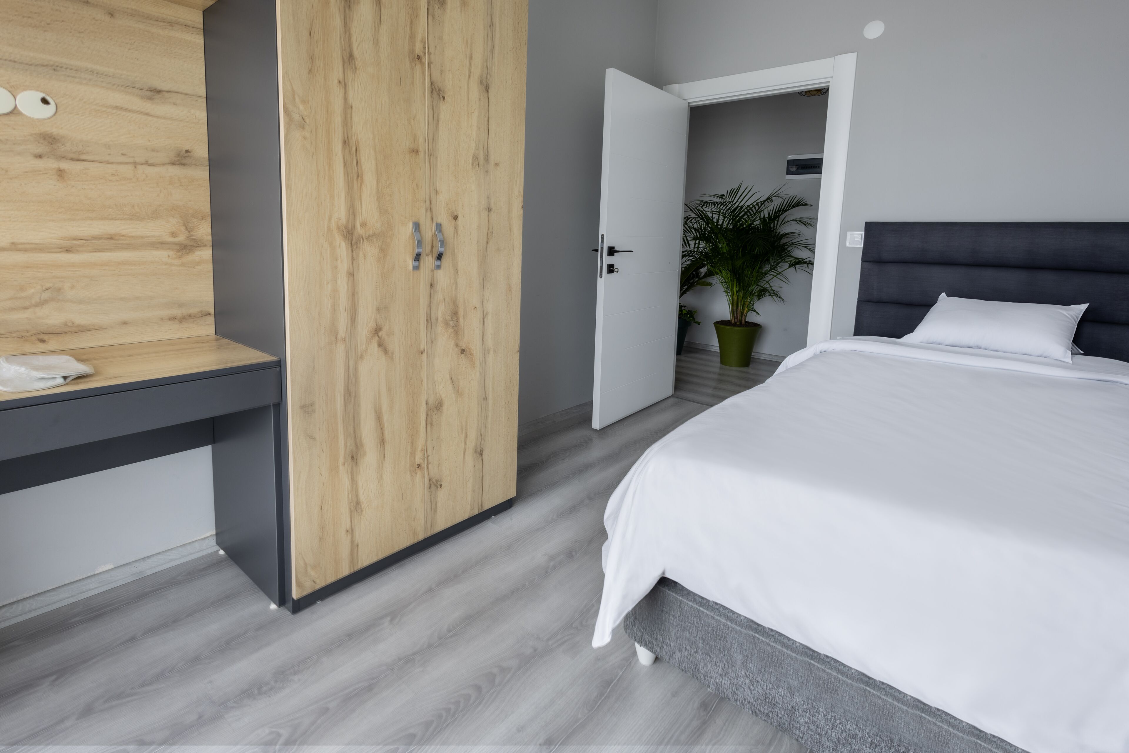 A bedroom with a bed, a wooden wardrobe, a desk, and a potted plant.