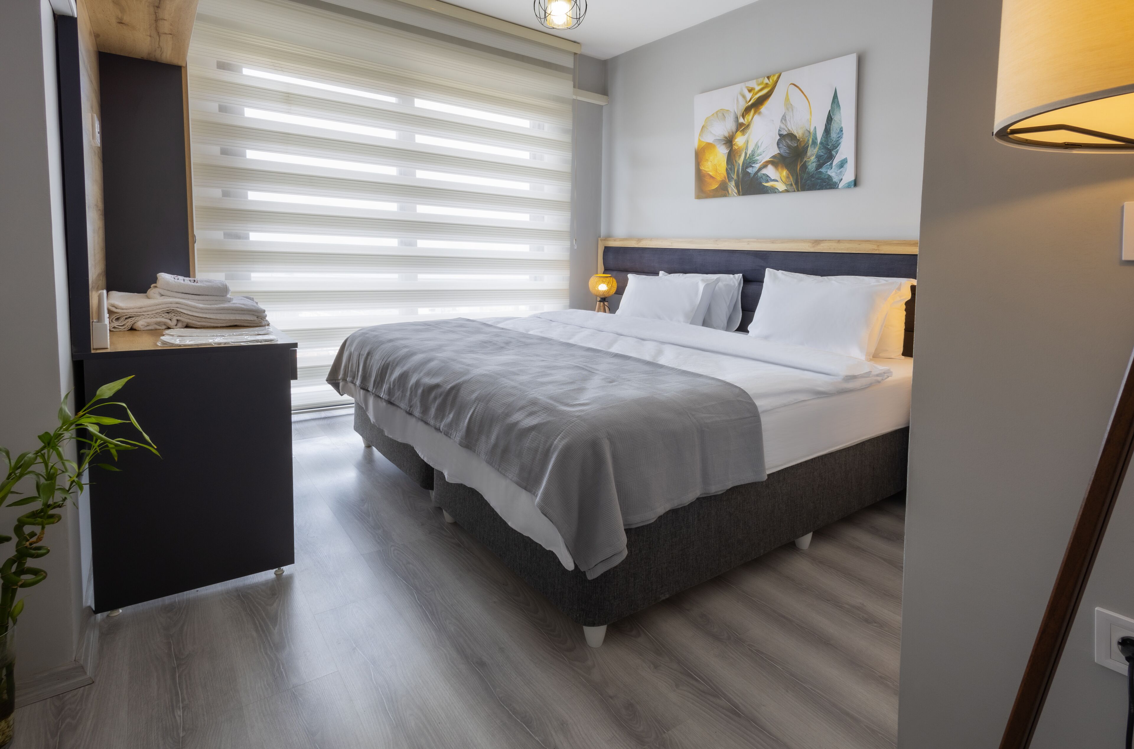 A modern bedroom with a bed, bedside table, and a window with blinds.