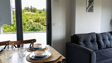 Zona pranzo con tavolo apparecchiato per quattro persone, un divano e vista sul verde.
