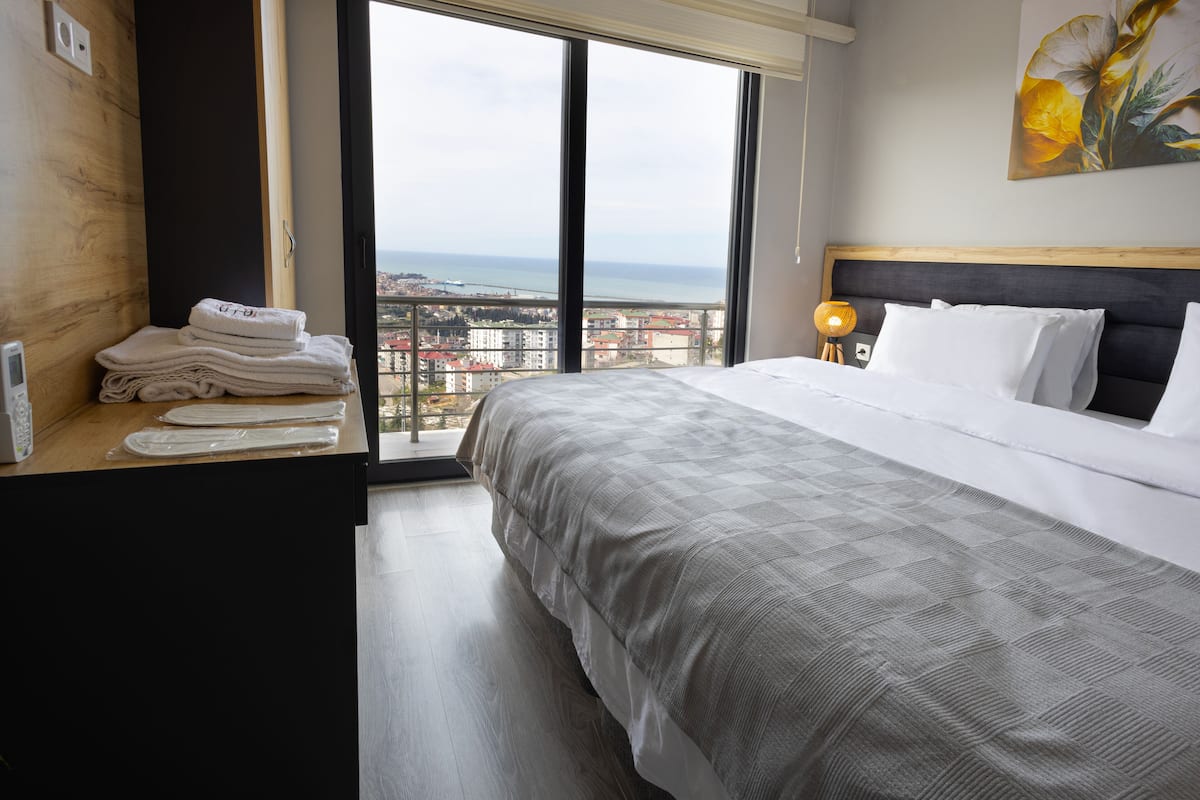 A hotel room with a large bed, a view of the city, and a wooden desk with towels.