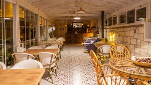A cozy restaurant with wooden tables and wicker chairs, a tiled floor, and a stone wall. - PANDA ALAÇATI OTEL (Cesme)