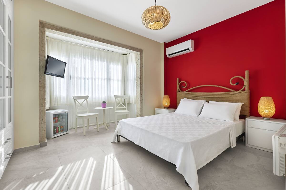 A bedroom with a bed, bedside tables, a TV, and a window with curtains.