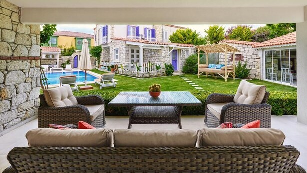 A patio with wicker furniture, a glass table, and a pool in the background. - PANDA ALAÇATI OTEL (Cesme)