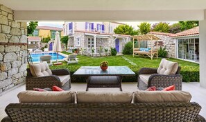 A patio with wicker furniture, a glass table, and a pool in the background. - PANDA ALAÇATI OTEL (Cesme)