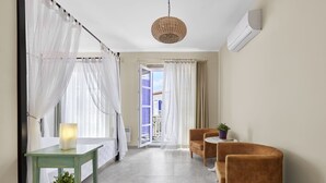 A modern hotel room with a bed, a small table with a lamp, two chairs, a potted plant, and a view of the outside balcony. - PANDA ALAÇATI OTEL (Cesme)
