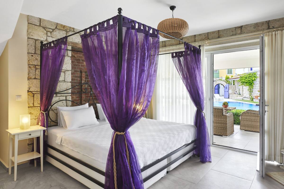 A bed with a canopy, a bedside table, and a view of an outdoor swimming pool.
