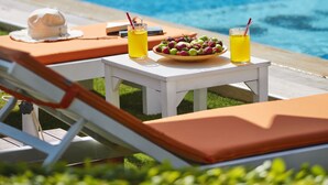 A poolside area with lounge chairs, a table with drinks and fruit, and a stone wall in the background. - PANDA ALAÇATI OTEL (Cesme)