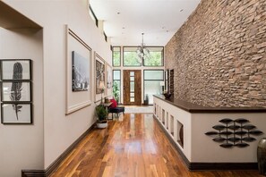 Un pasillo con suelo de madera, obras de arte enmarcadas, una pared de acento de piedra y un candelabro.