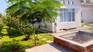 Ein modernes Haus mit weißer Fassade, einem großen Fenster und einem gepflegten Garten mit grünem Rasen und einer Palme.