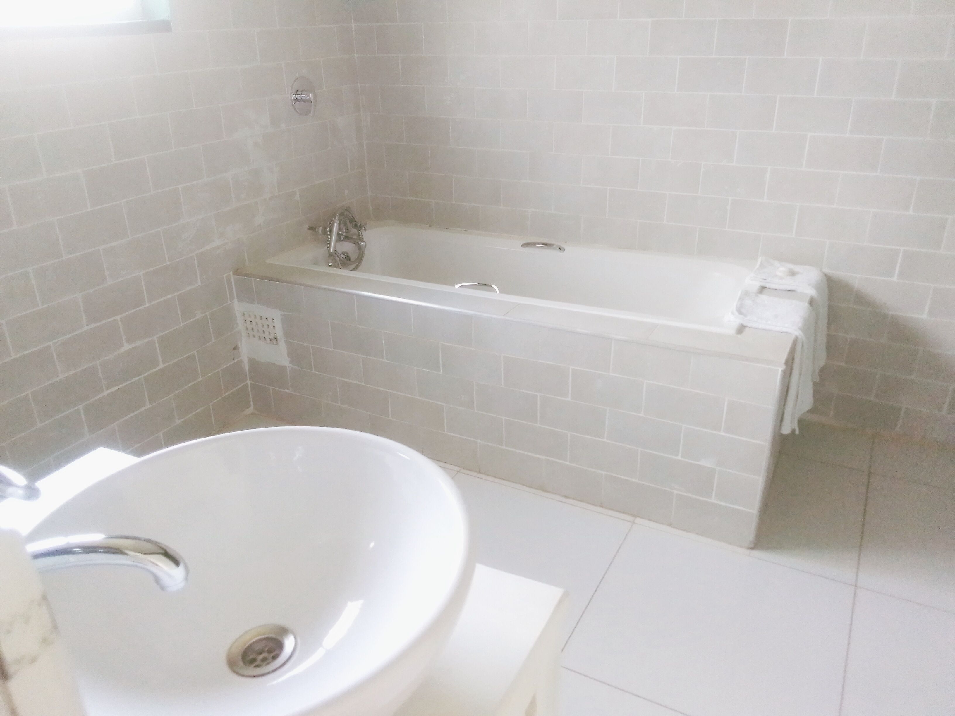 Une salle de bain avec une baignoire blanche, un lavabo blanc et un sol carrelé.