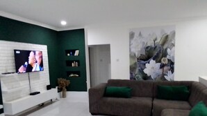 Ein modernes Wohnzimmer mit einer weißen Unterhaltungseinheit, einem braunen Sofa mit grünen Kissen und einem großen floralen Kunstwerk an der Wand, sowie einer grünen Akzentwand.