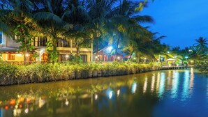 A waterfront hotel with a canal, palm trees, and illuminated buildings.