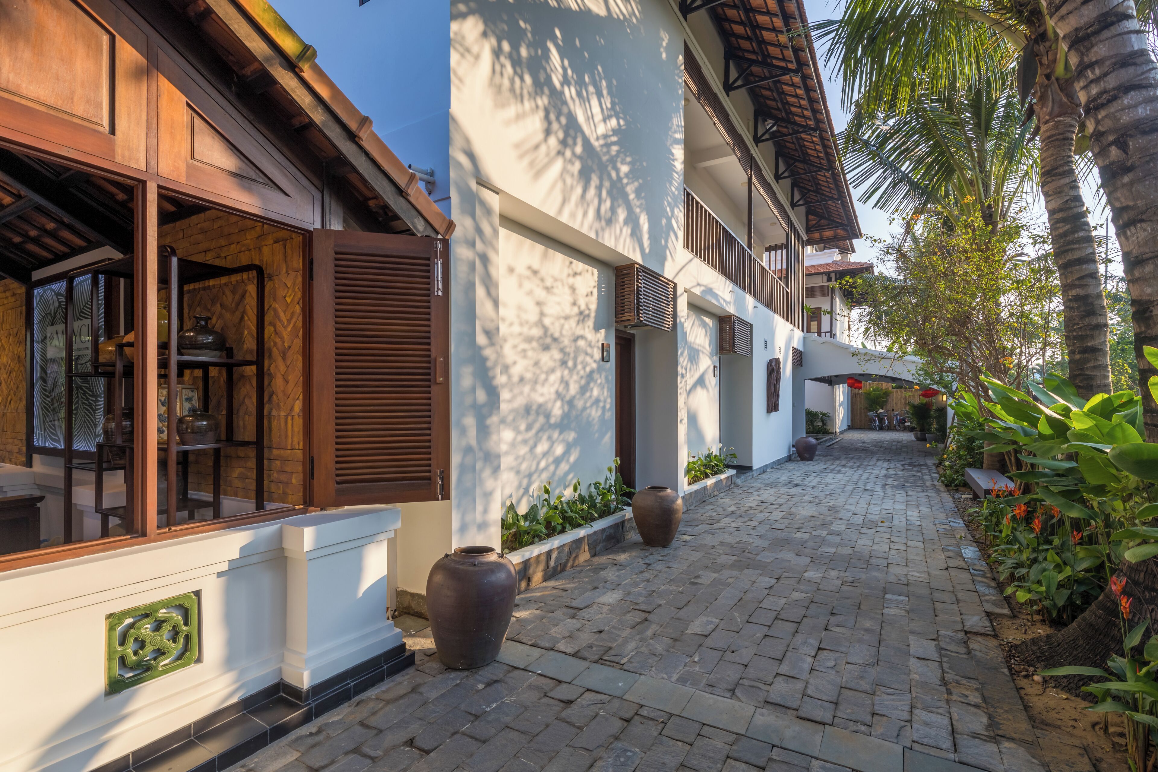 A paved pathway flanked by buildings with wooden shutters and large vases.
