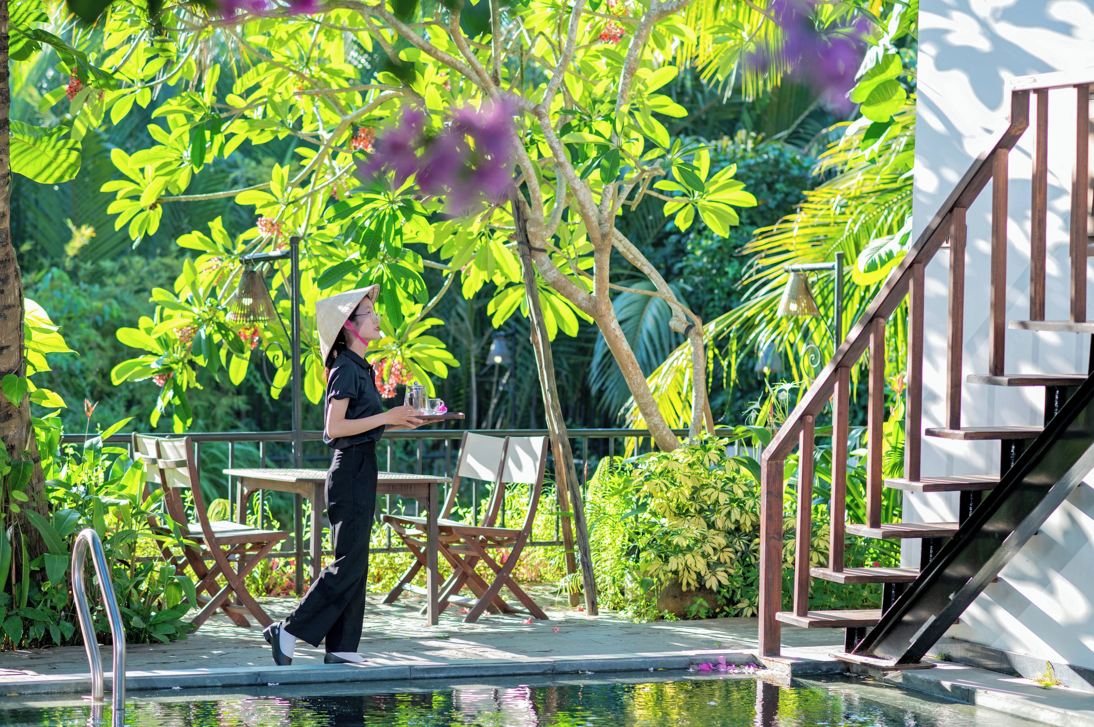 A poolside area with a wooden staircase, outdoor seating, and lush greenery.