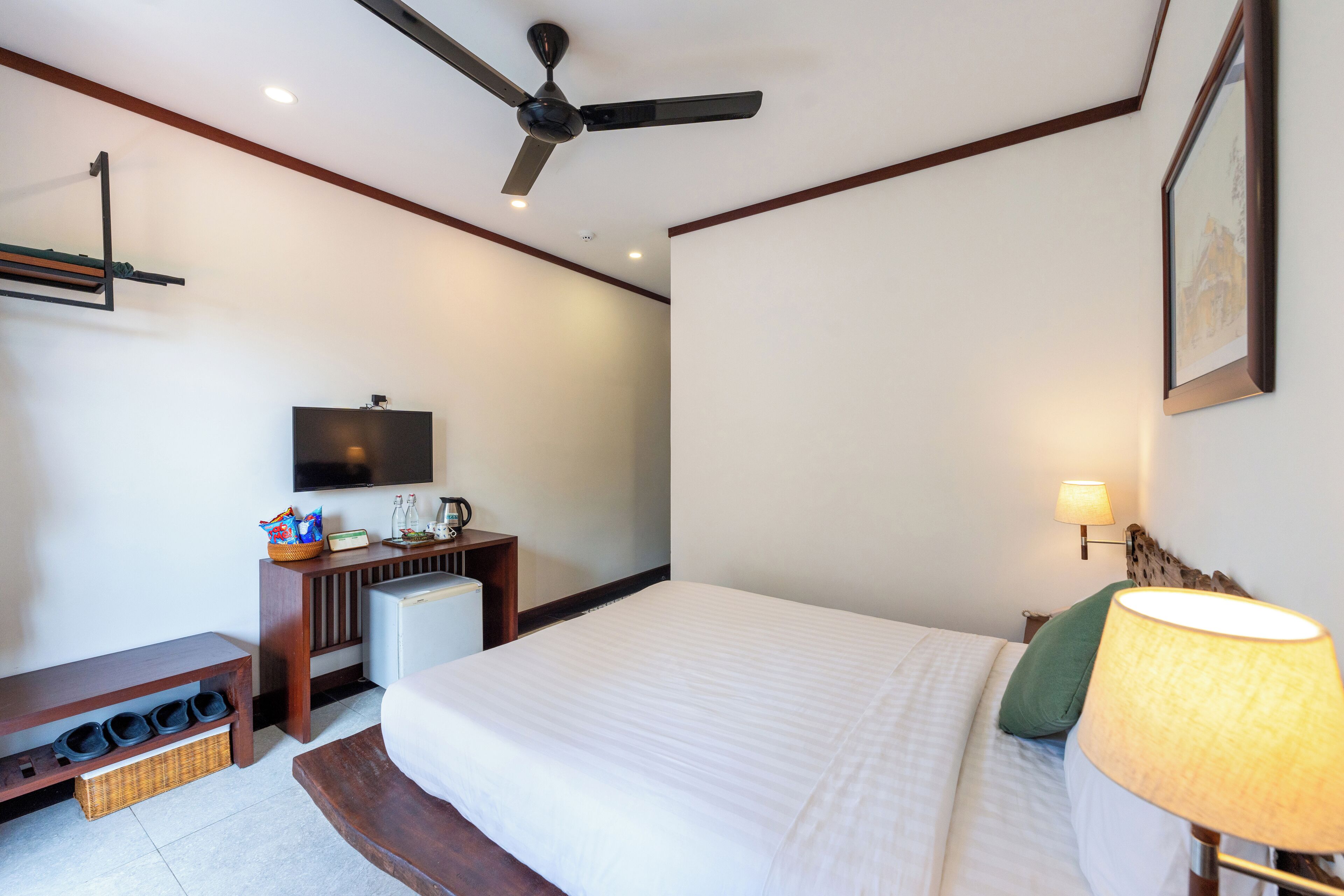 A hotel room with a bed, a desk, a television, and a ceiling fan.