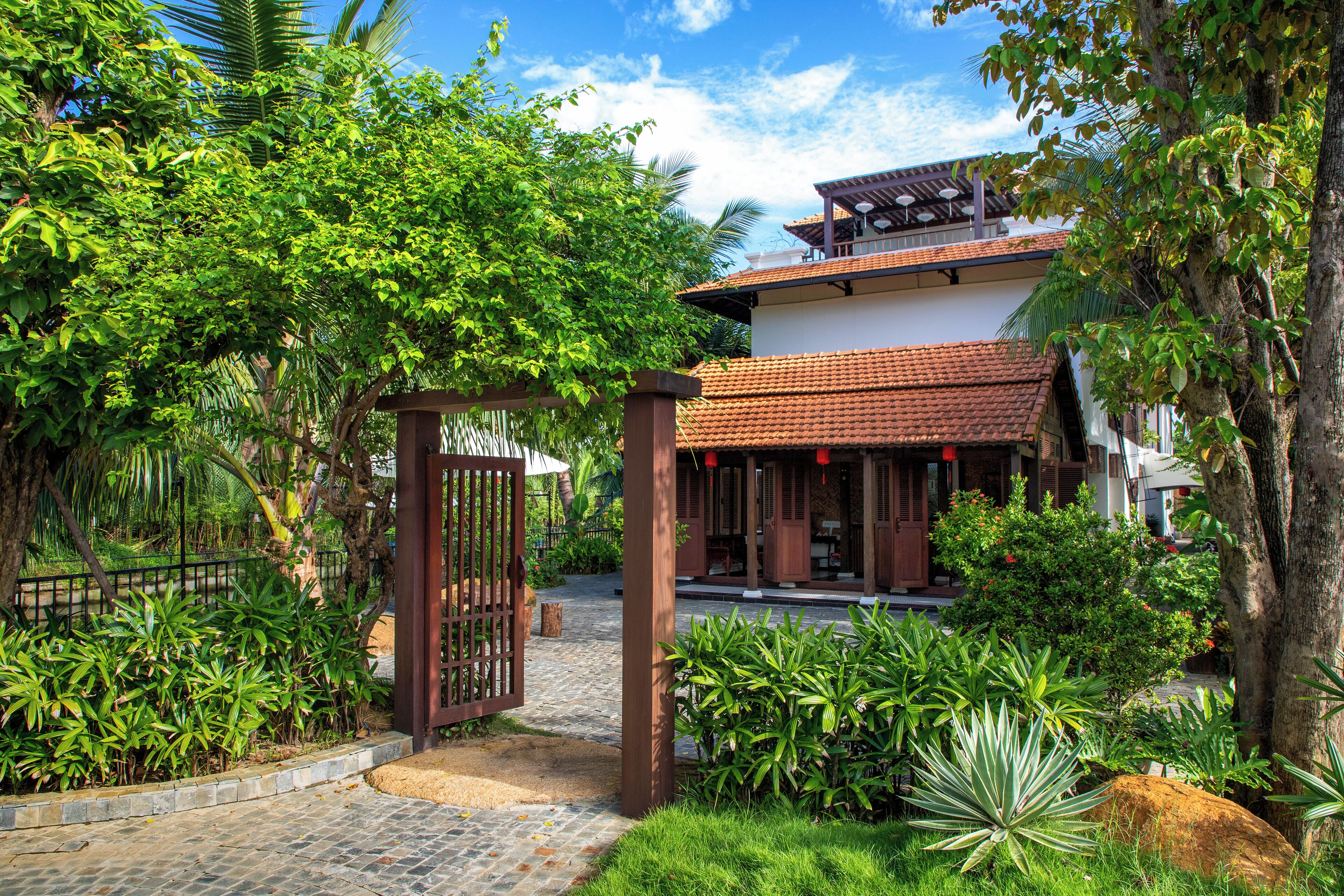 A traditional house with a tiled roof, surrounded by lush greenery and a stone pathway leading to the entrance.