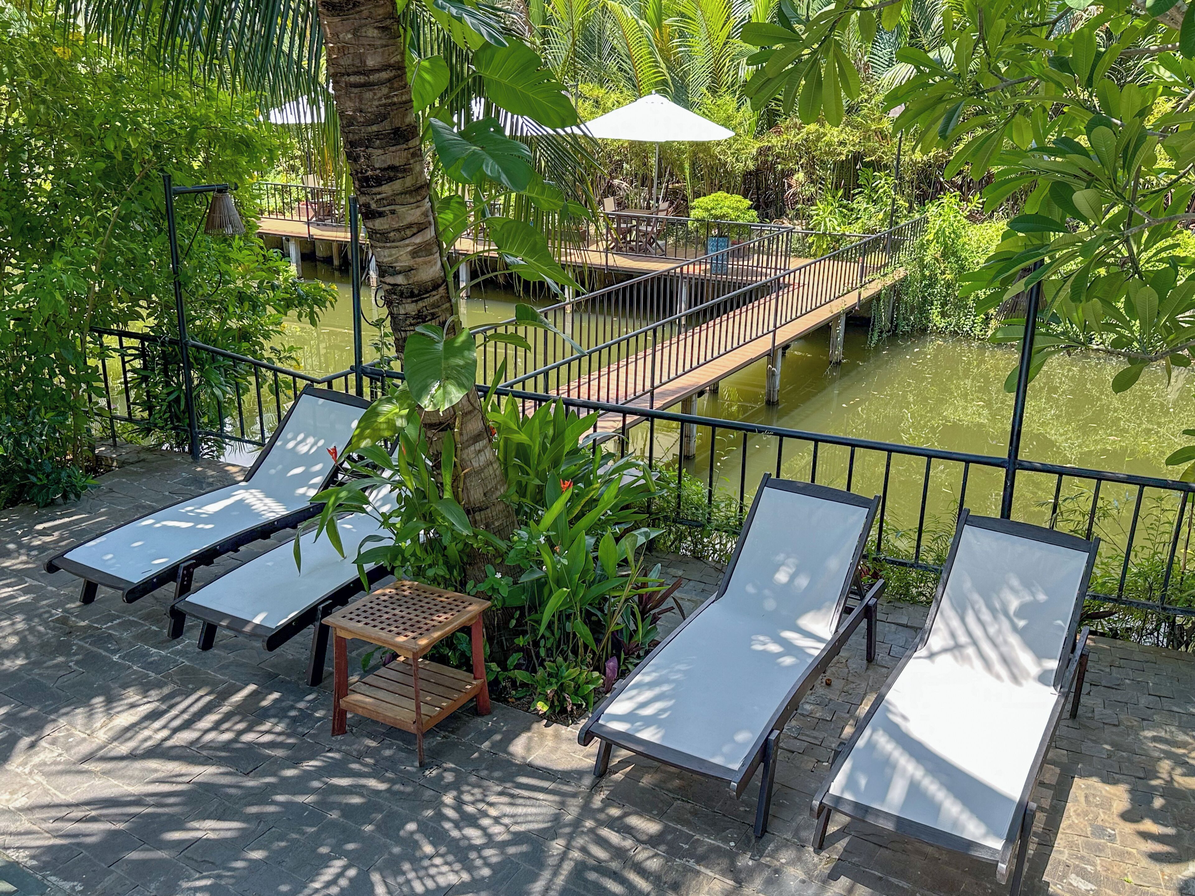 A patio area with lounge chairs, a small table, and a wooden deck over a pond.
