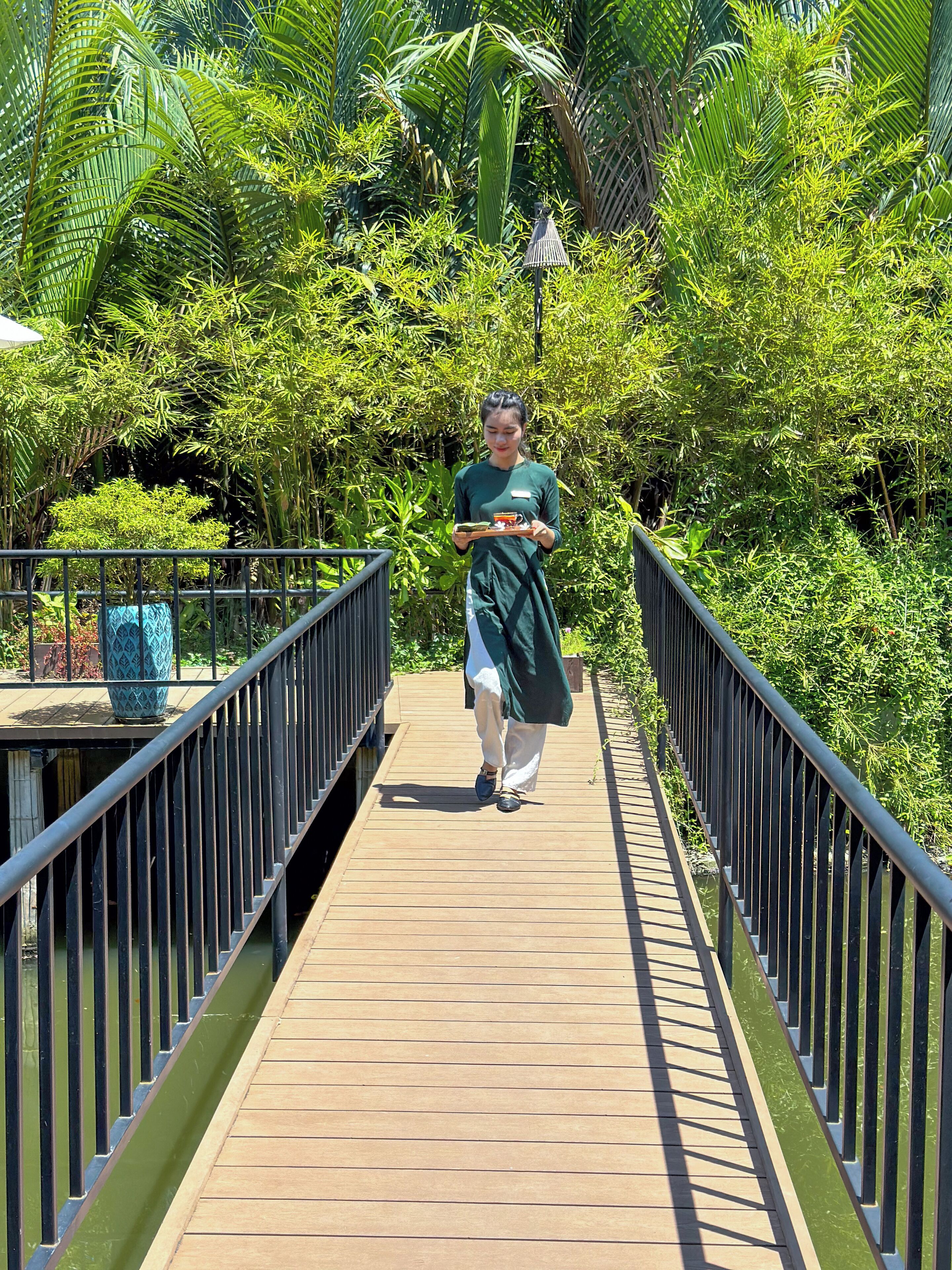 Una persona camina sobre un pont de fusta envoltat de vegetació abundant.