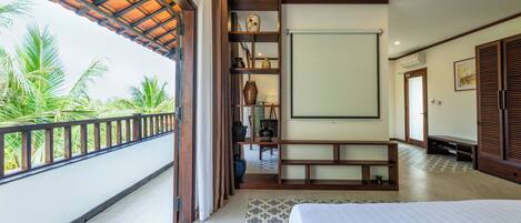 Habitación de hotel con balcón, una cama, repisas de madera con adornos y vista a palmeras.