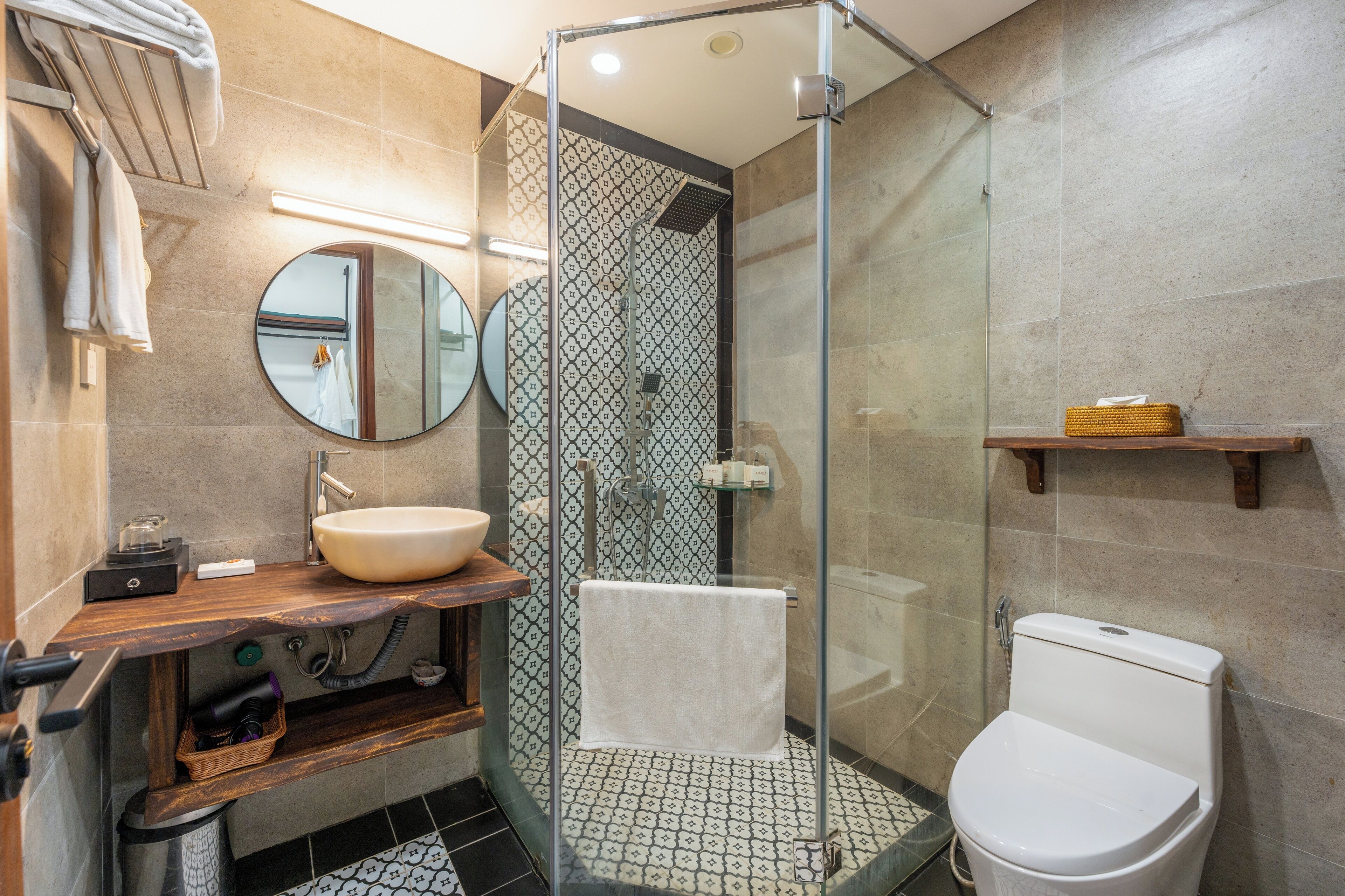 Een moderne badkamer met een douchecabine van glas, een ronde spiegel, een wastafel en een toilet.