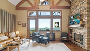 Amplia sala de estar con chimenea de piedra, ventanas grandes y un rincón de descanso acogedor.