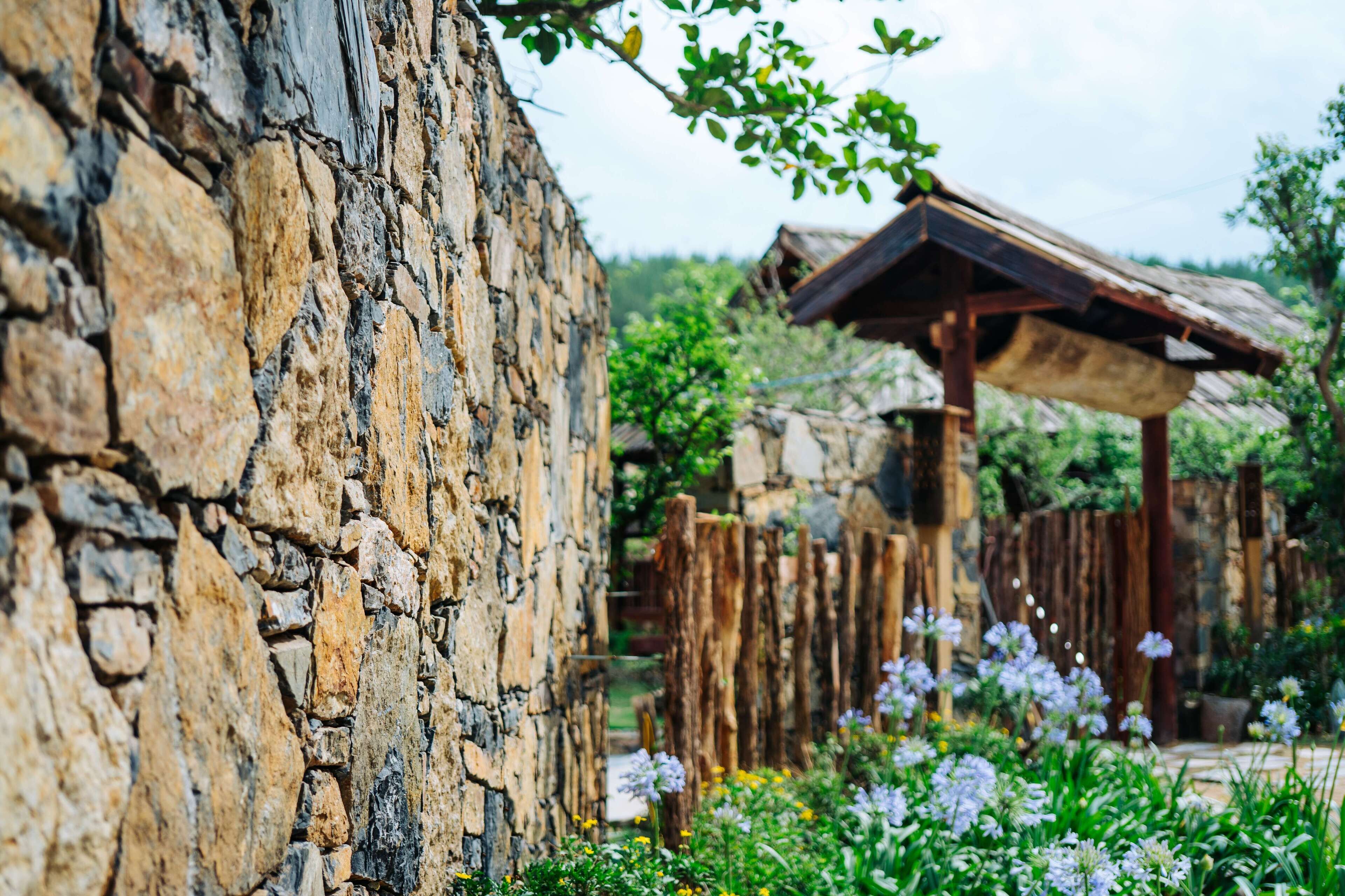 Un muro de piedra rústico con una valla de madera y una estructura de techo de paja.