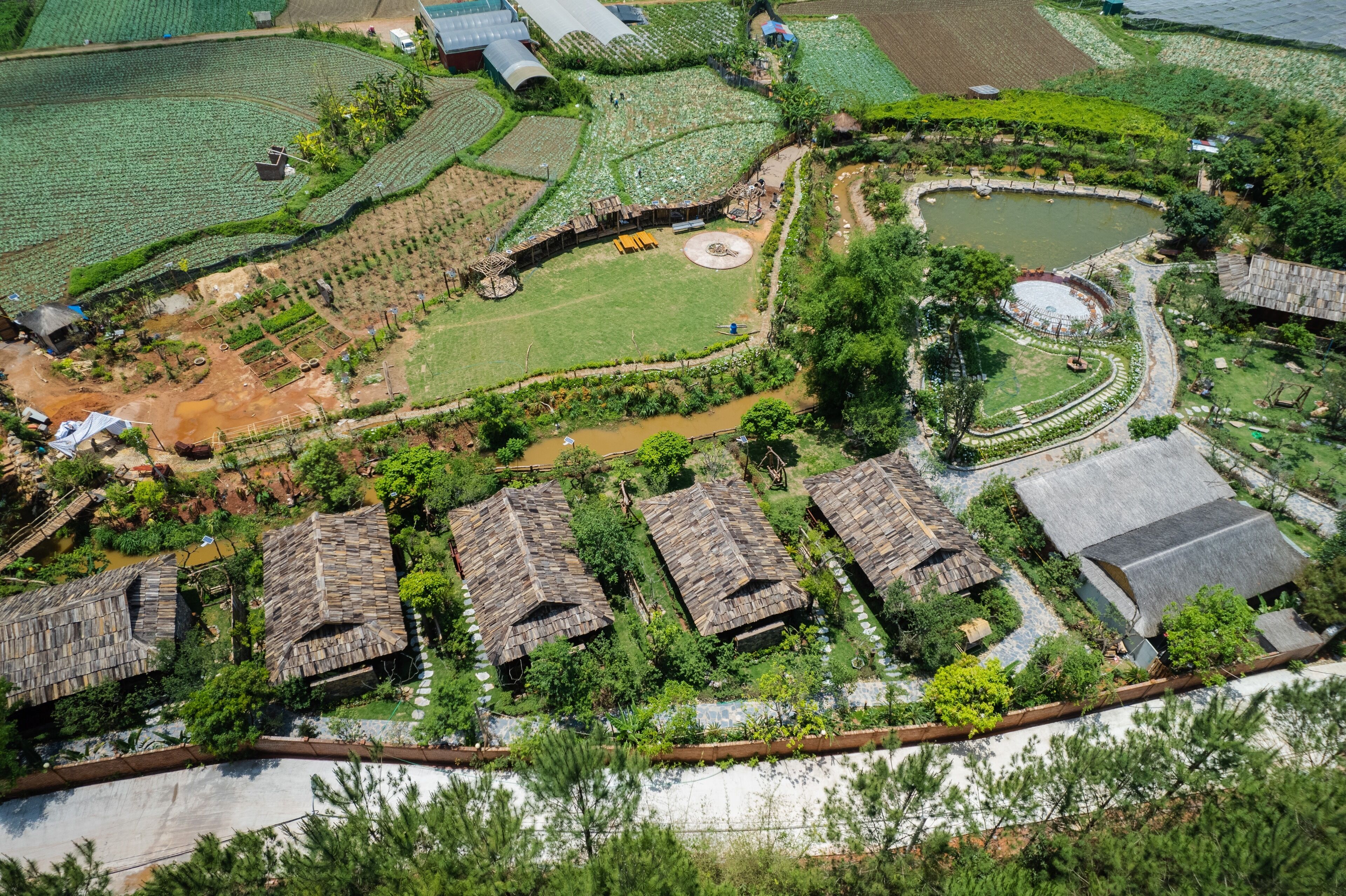 An aerial view of a rural area with terraced fields, a pond, and traditional thatched-roof houses.