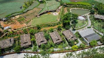 An aerial view of a rural area with terraced fields, a pond, and traditional thatched-roof houses.