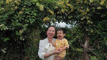 A person holding a child under a leafy archway in a natural setting.