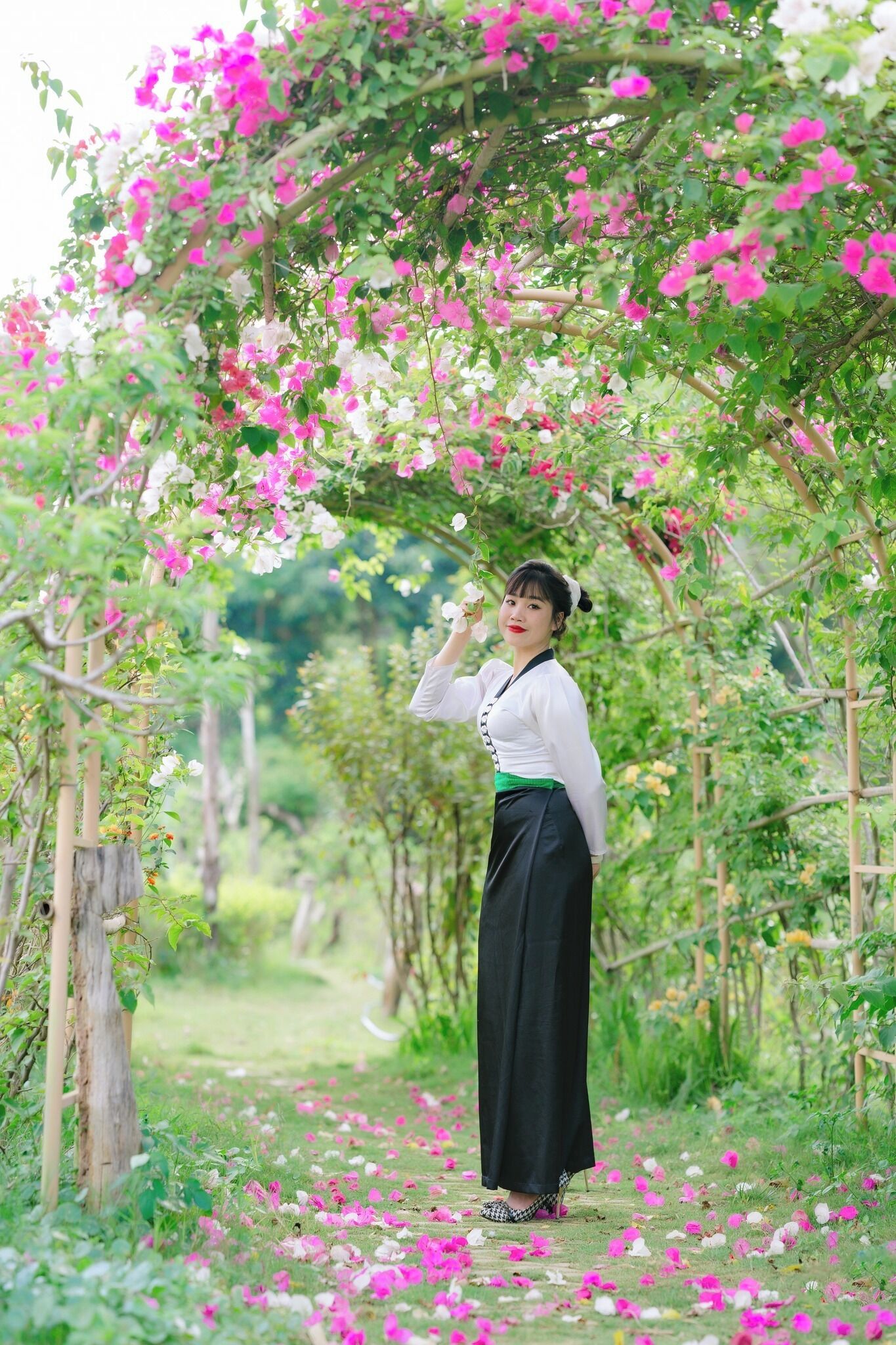 A woman standing under a floral archway in a garden.