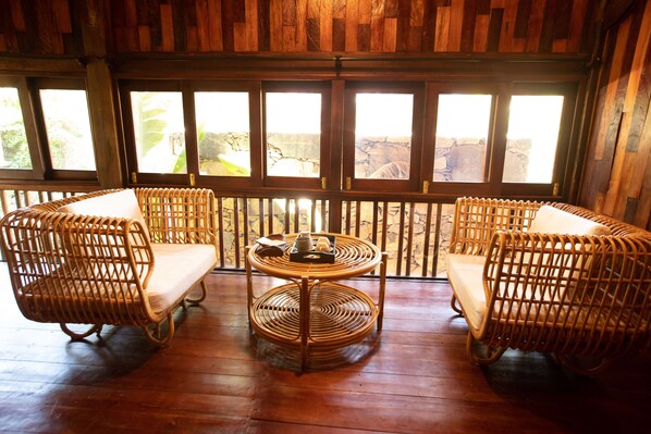 A wooden-floored room with two wicker chairs and a small round table, large windows with a view of greenery and a rocky landscape. - Natalie's Villa & Resort Moc Chau (Moc Chau)