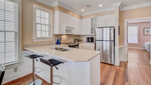 A modern kitchen with white cabinets, a stainless steel refrigerator, and a central island with bar stools. - Steps to Two Oceanfront Pools | Walk to Dining | Grand Pavilion (Isle of Palms)