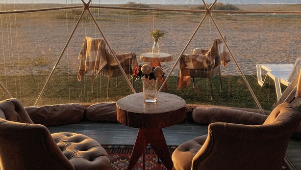 Un área con carpas y vista al paisaje, amoblada con sillas y una mesa, y un tapete estampado en el suelo.