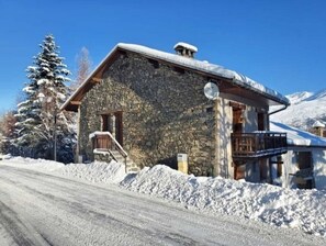 Un edifici de pedra amb un teulat cobert de neu, unes escales de fusta i una antena satèl·lit.