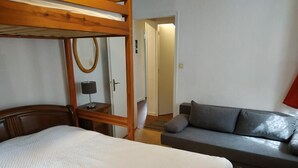 Ein Zimmer mit einem Etagenbett, einer Schlafcouch, einem Nachttisch mit Lampe und einem Spiegel.
