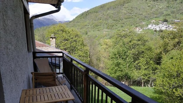 Ein Balkon mit Tisch und Stühlen, der einen Blick auf eine Berglandschaft mit einem Dorf in der Ferne bietet.