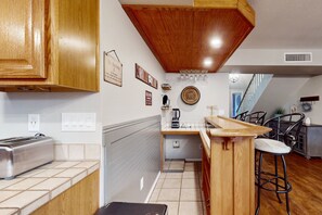 A kitchen with wooden cabinets, a built-in toaster, a coffee maker, and a bar area with stools. - Fun-filled, modern home with game room, heated pool, hot tub, grill (Chandler)