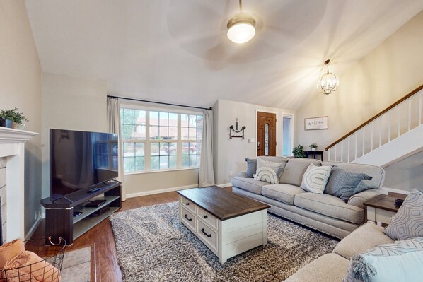 A living room with a flat-screen TV, a sofa, a coffee table, and a staircase. - Fun-filled, modern home with game room, heated pool, hot tub, grill (Chandler)
