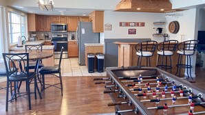 Une cuisine moderne avec des meubles en bois, une table de baby-foot et un coin bar avec des tabourets.