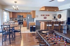 A modern kitchen with wooden cabinets, a foosball table, and a bar area with stools. - Fun-filled, modern home with game room, heated pool, hot tub, grill (Chandler)