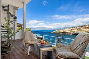 A balcony with two beige chairs, a small table with drinks, and a potted plant. - Nieva Apartment 1 (Matala)