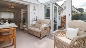 Un salon chaleureux, meublé de meubles en osier, avec une table à manger dressée avec des assiettes et des verres, et une grande porte vitrée donnant sur l’extérieur.