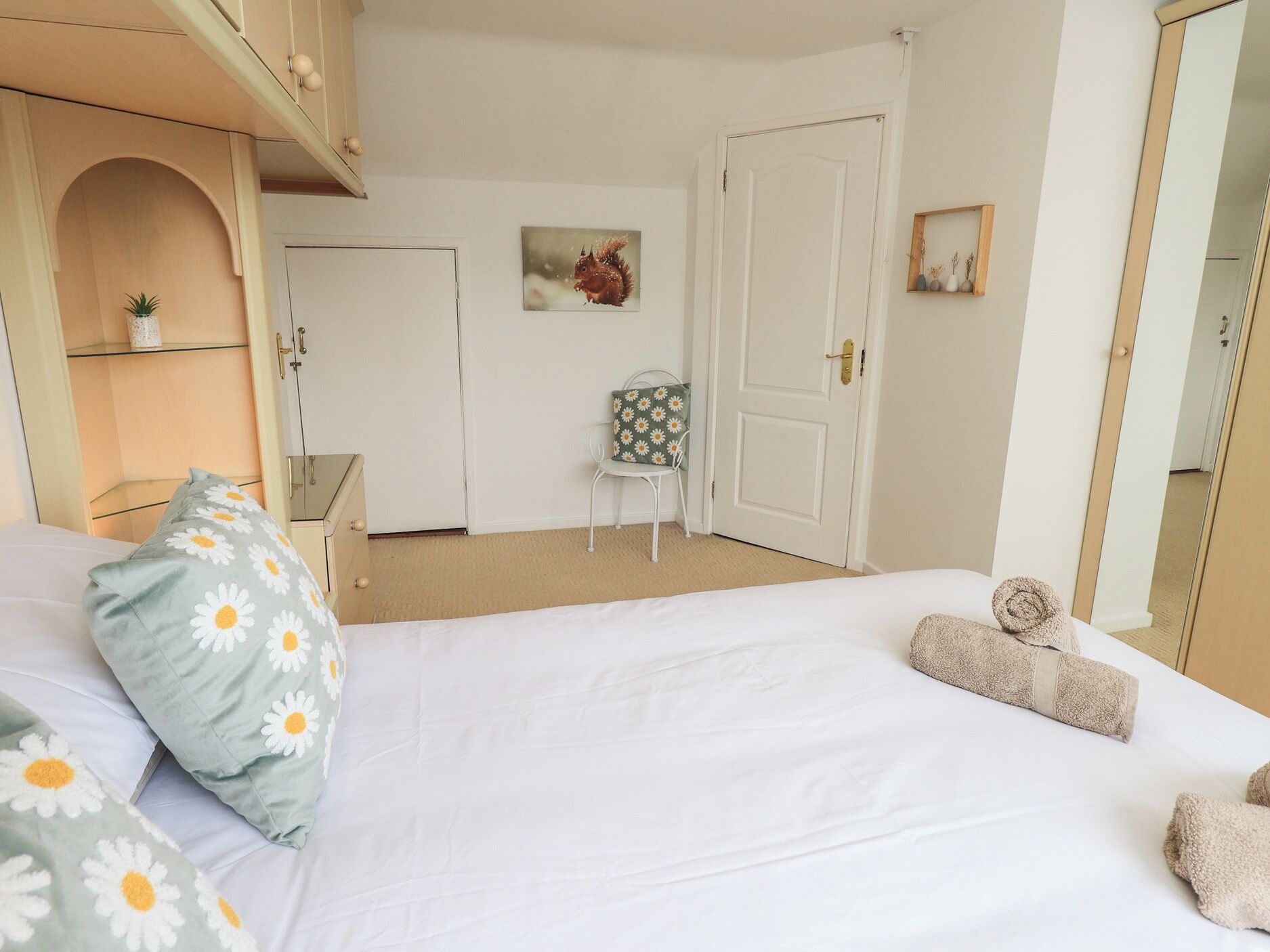 A bedroom with a bed, pillows, a chair, a door, and a mirror.